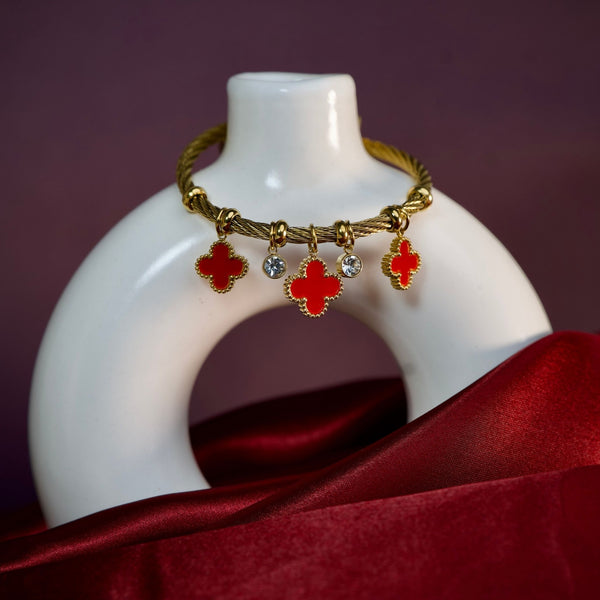 Red charm bracelet by Sajna Sawarnaa with gold finish and lucky clover accents, featuring stylish jewelry design.