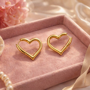 Pair of minimalist gold heart-shaped hoop earrings elegantly resting inside a plush pink velvet jewelry box.