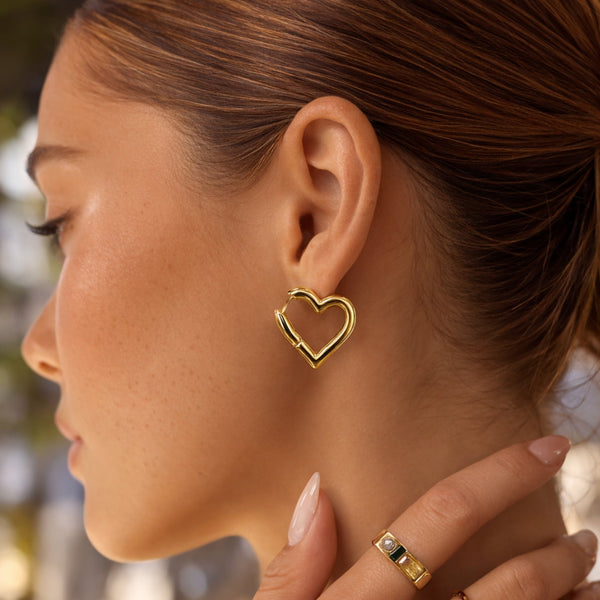 Close-up profile of a woman wearing modern gold heart hoop earrings, styled for an everyday chic look.