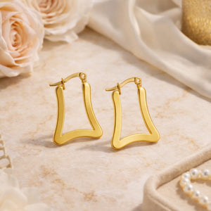 Gold geometric trapeze hoop earrings on marble surface with roses – lifestyle product shot by Sajna Sawarnaa