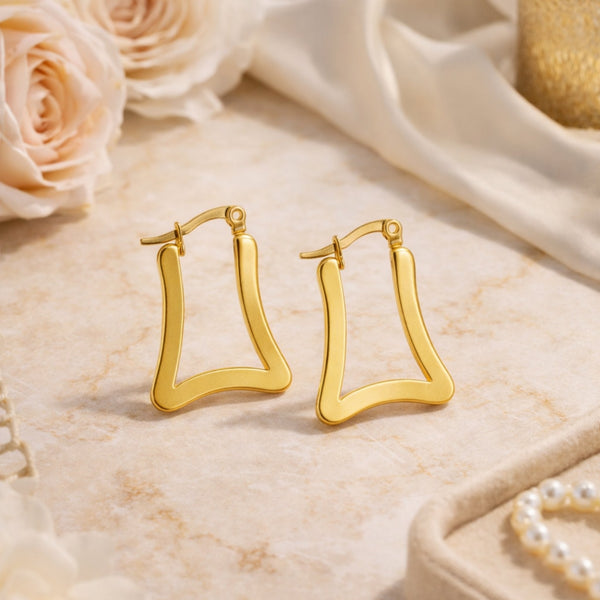 Gold geometric trapeze hoop earrings on marble surface with roses – lifestyle product shot by Sajna Sawarnaa