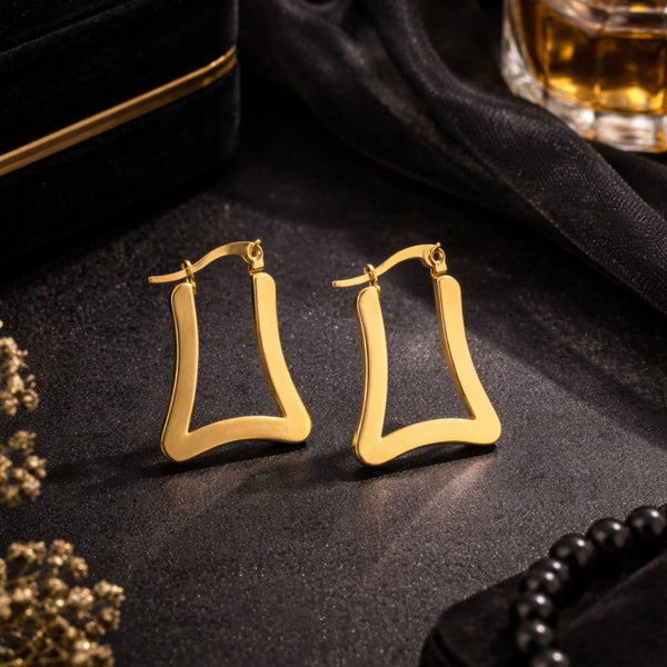 Chunky gold-tone trapeze hoop earrings on dark velvet luxury background – editorial mood shot