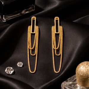 Triple-layer gold cascade chain drop earrings on black satin with crystals – luxury editorial mood shot