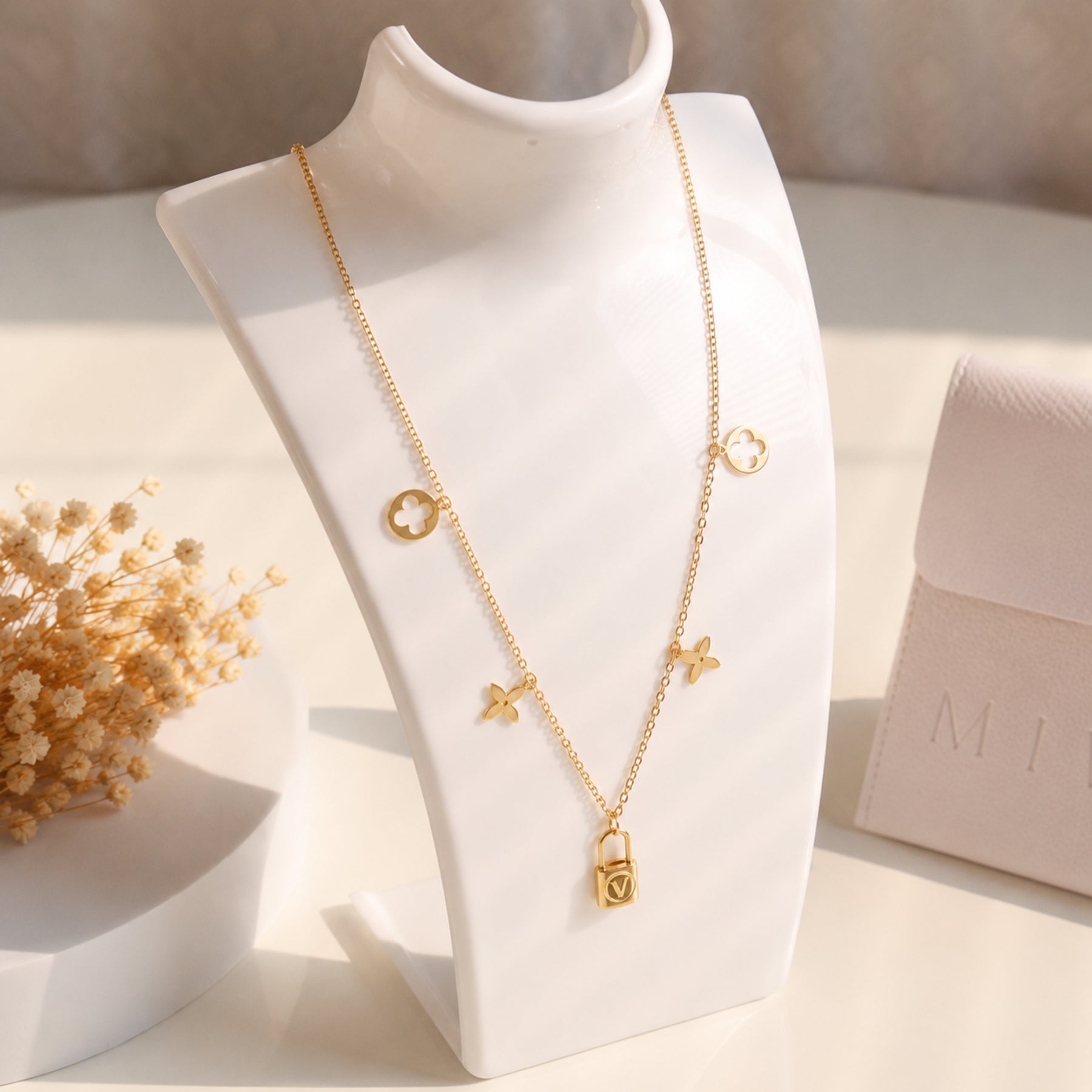 Gold clover and lock charm necklace displayed on a jewellery bust