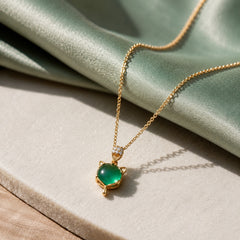Gold-tone green cat charm necklace styled on a soft green editorial background