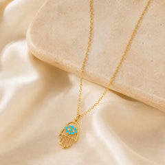 Gold-tone turquoise-accent Hamsa hand charm necklace on a soft editorial background
