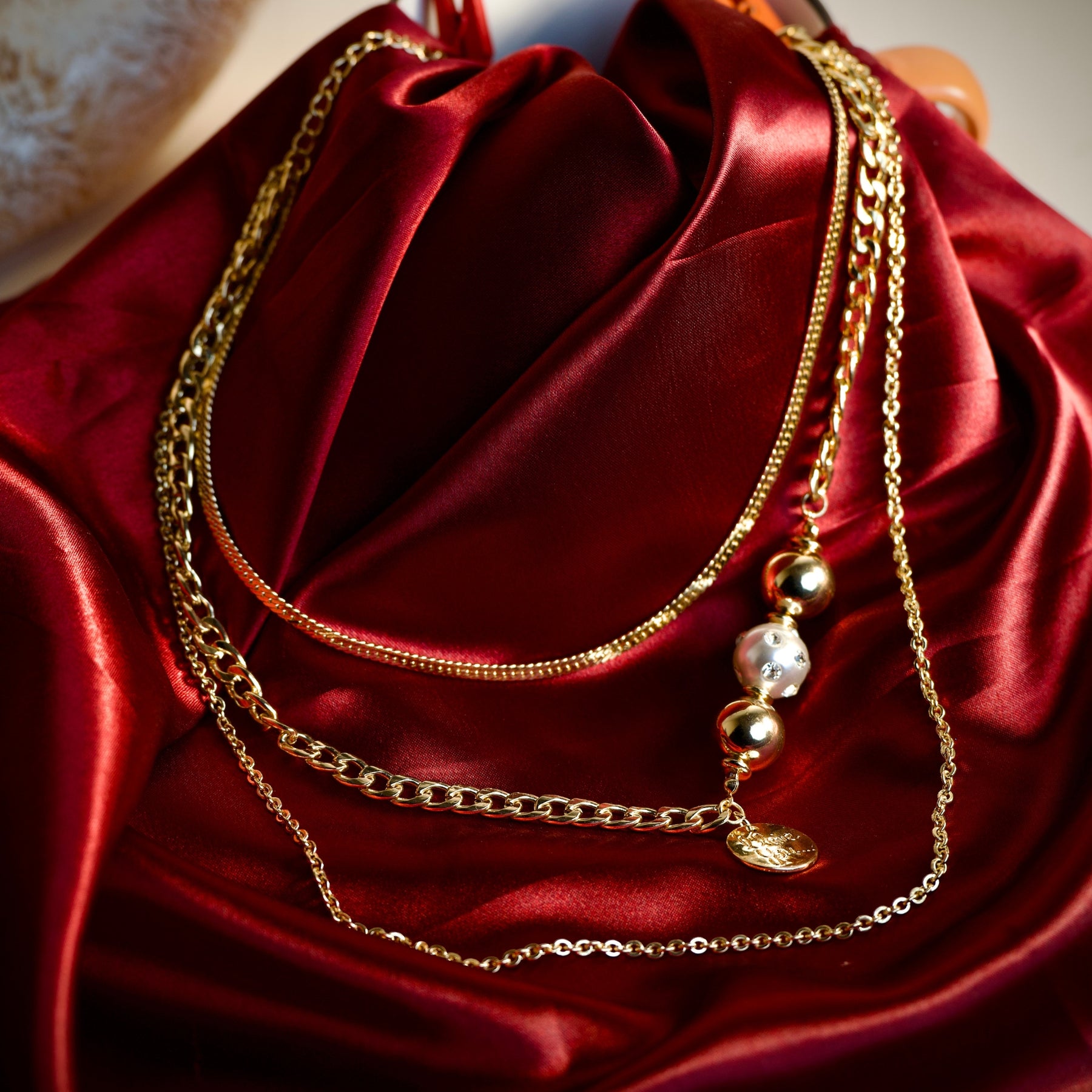 Layered gold-tone bead and message charm necklace styled on a red editorial background