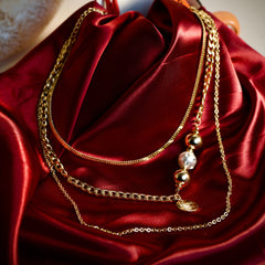 Layered gold-tone bead and message charm necklace styled on a red editorial background