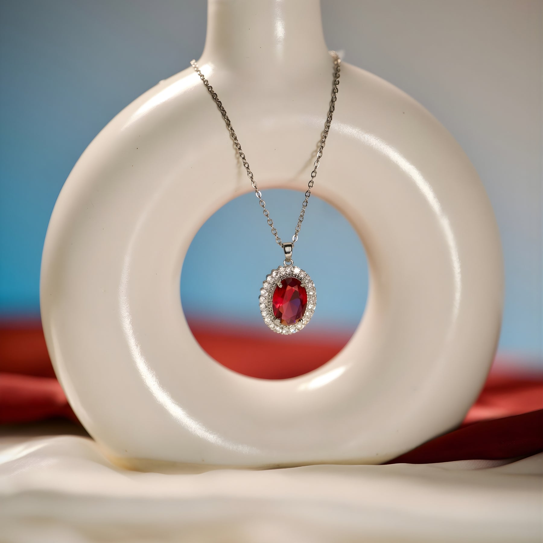 Silver-tone red stone-accent oval pendant necklace styled on an editorial background