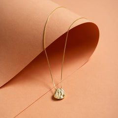 Gold-tone organic pendant necklace styled on a warm editorial background