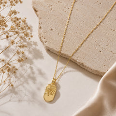 Gold-tone sunburst pendant necklace styled on a neutral editorial background