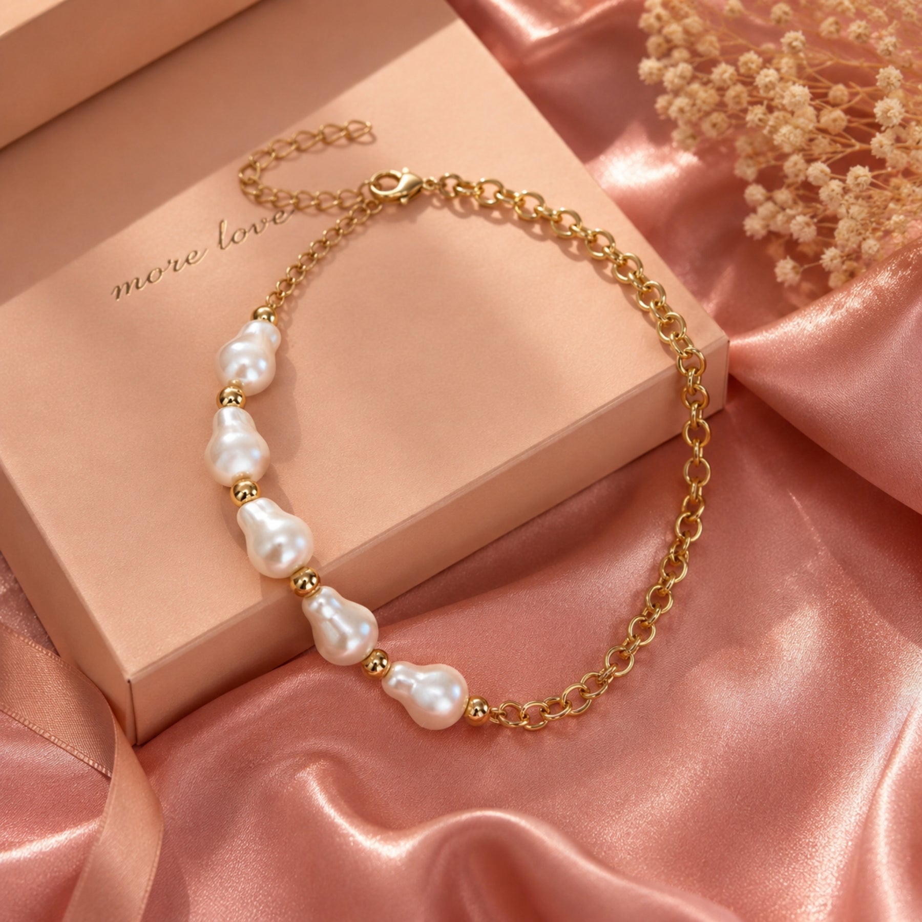 Gold-tone chain necklace with irregular pearl accents styled on a pink editorial background