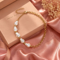 Gold-tone chain necklace with irregular pearl accents styled on a pink editorial background