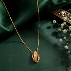Gold-tone openwork pendant necklace with clear stone accents on a green editorial background