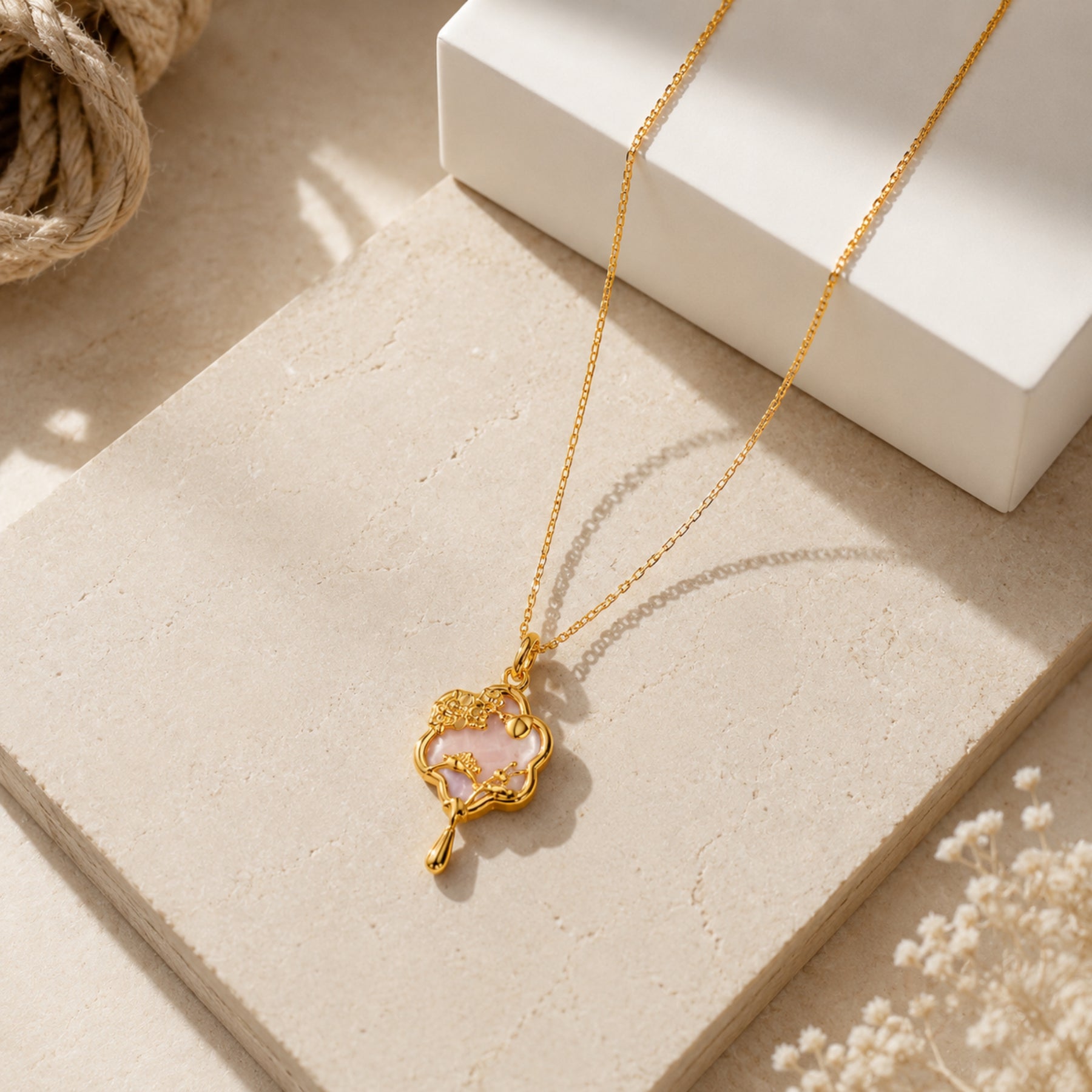 Gold-tone pink floral charm pendant necklace styled on a neutral editorial background