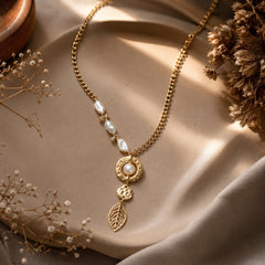 Gold-tone pearl-accent leaf drop necklace styled on a warm editorial background