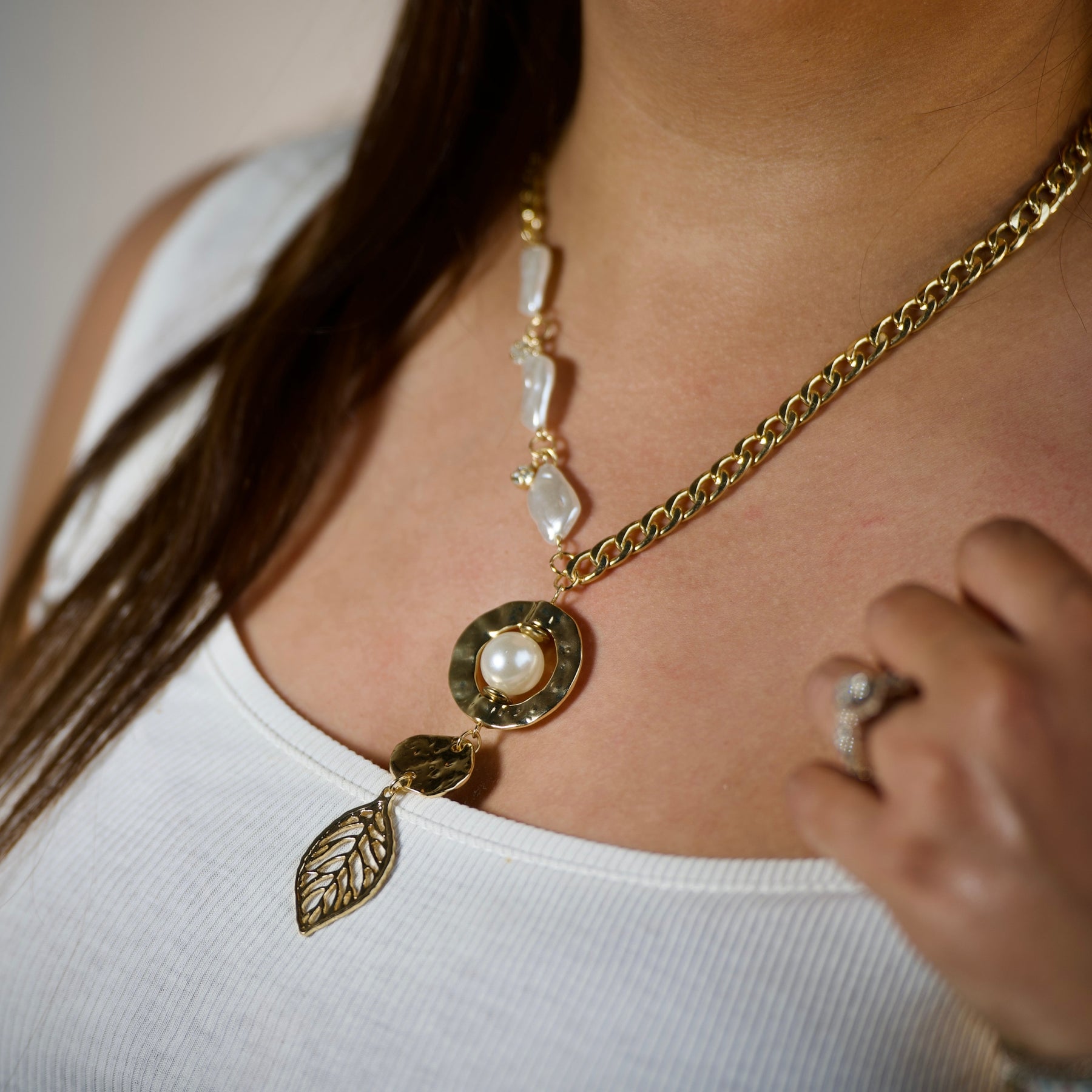 Close-up of a gold-tone pearl-accent leaf drop necklace worn by a woman