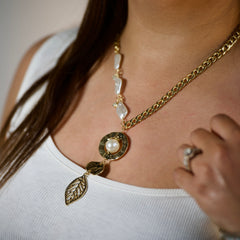 Close-up of a gold-tone pearl-accent leaf drop necklace worn by a woman