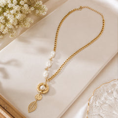 Gold-tone pearl-accent leaf drop necklace styled on a light editorial background